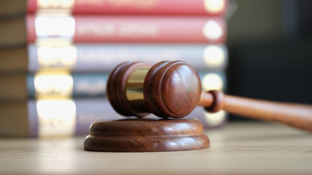 A Close Up of a Judge’s Gavel With a Stack of Law Books in the Background.