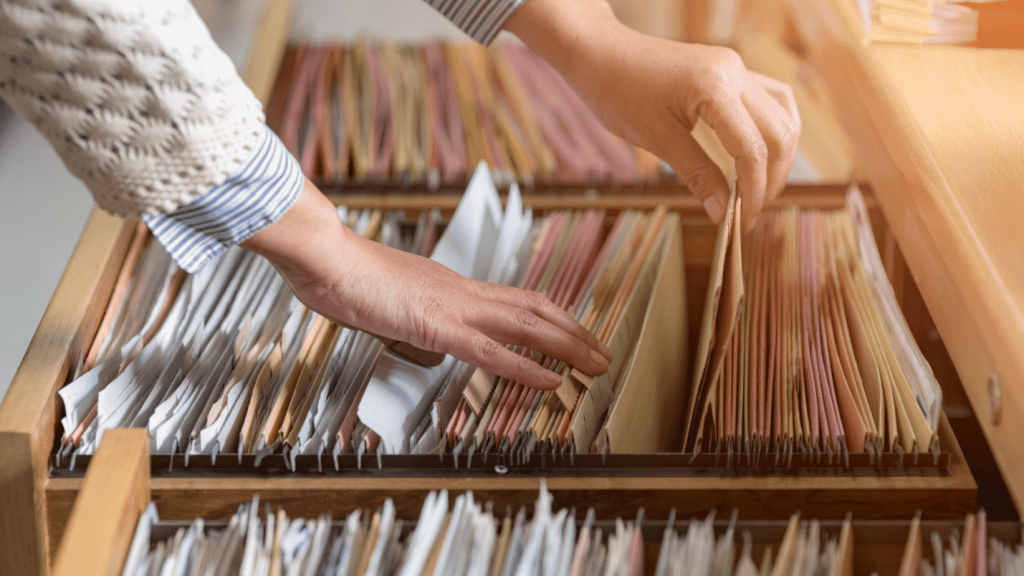 A person pulls a document out of a crowded file cabinet full of other documents.