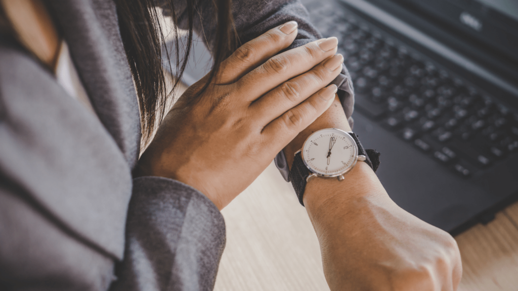 A person sits near a computer and checks their watch.