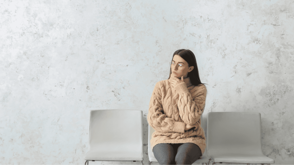 A woman sits on a chair in a waiting area looking pensive.