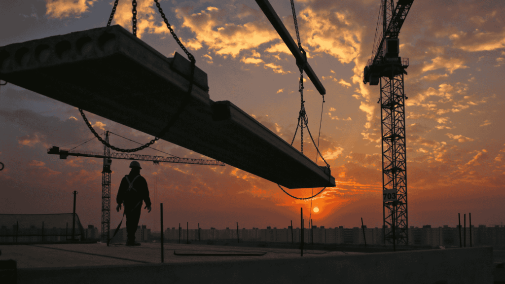 A construction site at sunset where a crane is lifting heavy materials.