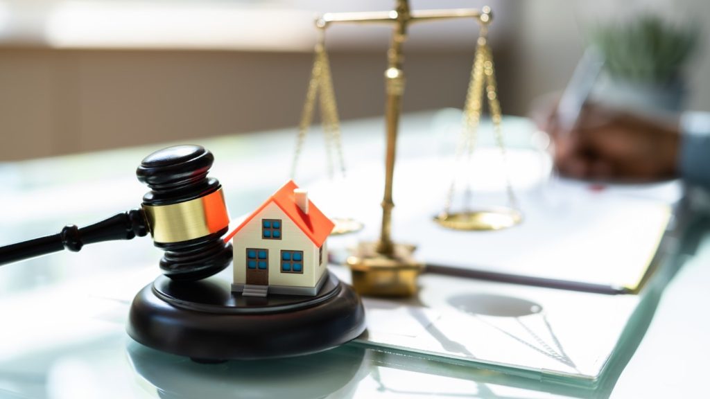 A set of scales, a gavel, a small model home all atop a desk.