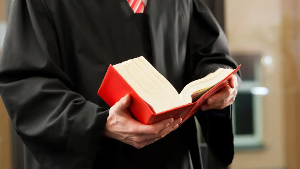A judge in black robes looks a large legal book.