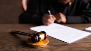 A judge signs a document at a large desk where a gavel rests. A judge signs a document at a large desk where a gavel rests.