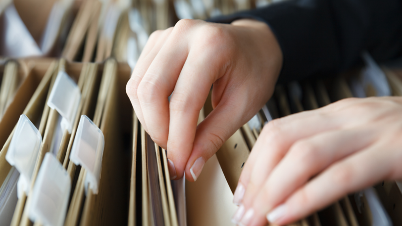 Hands searching through files in a filing cabinet for a legal document.