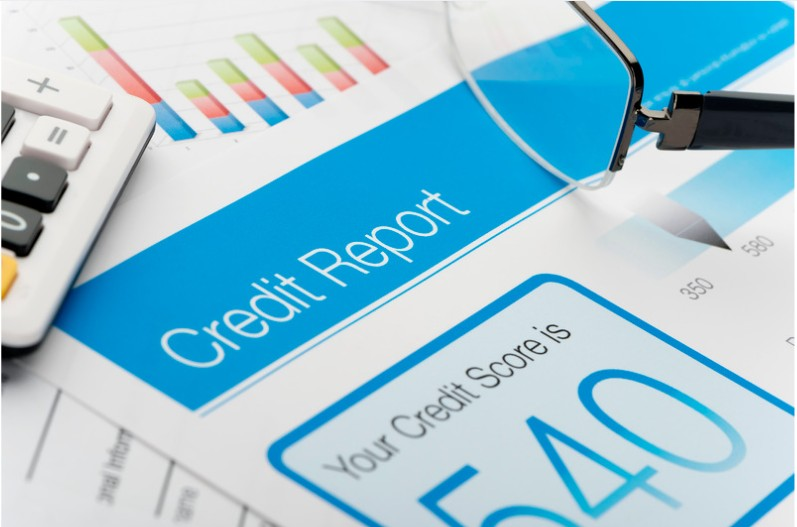 A credit report with a 540-credit score printed onto a piece of paper in blue ink with black frame glasses and the bottom of a calculator lying on top.